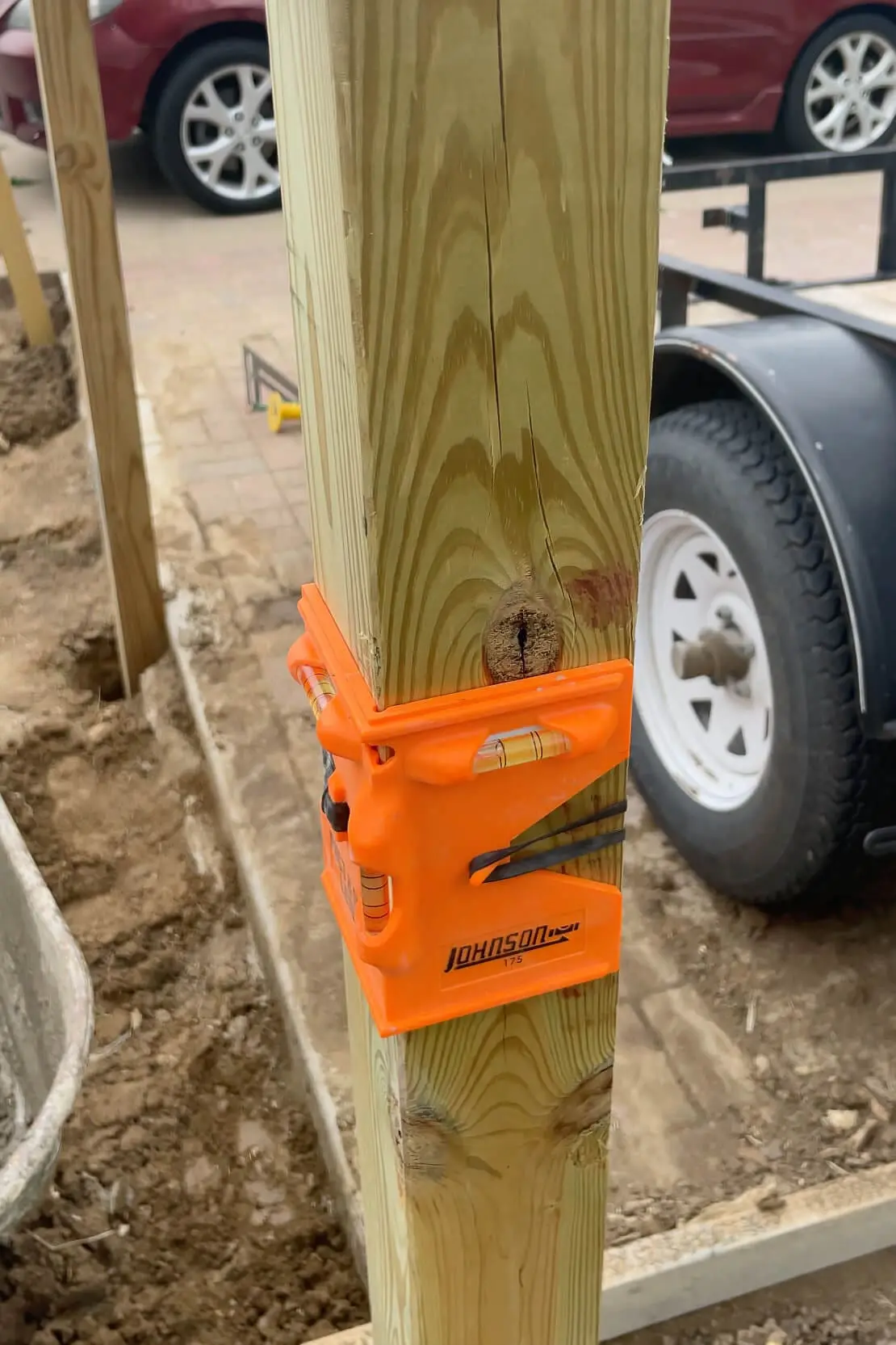 Bright orange post level tool used to align a pressure-treated wooden post while building a fence.